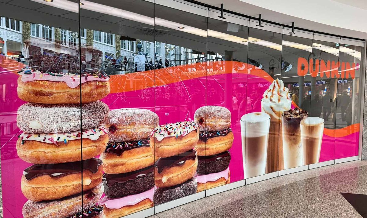 Foliertes Schaufenster eines Dunkin' Standorts mit Donut-Stapeln und Getränken auf Pink
