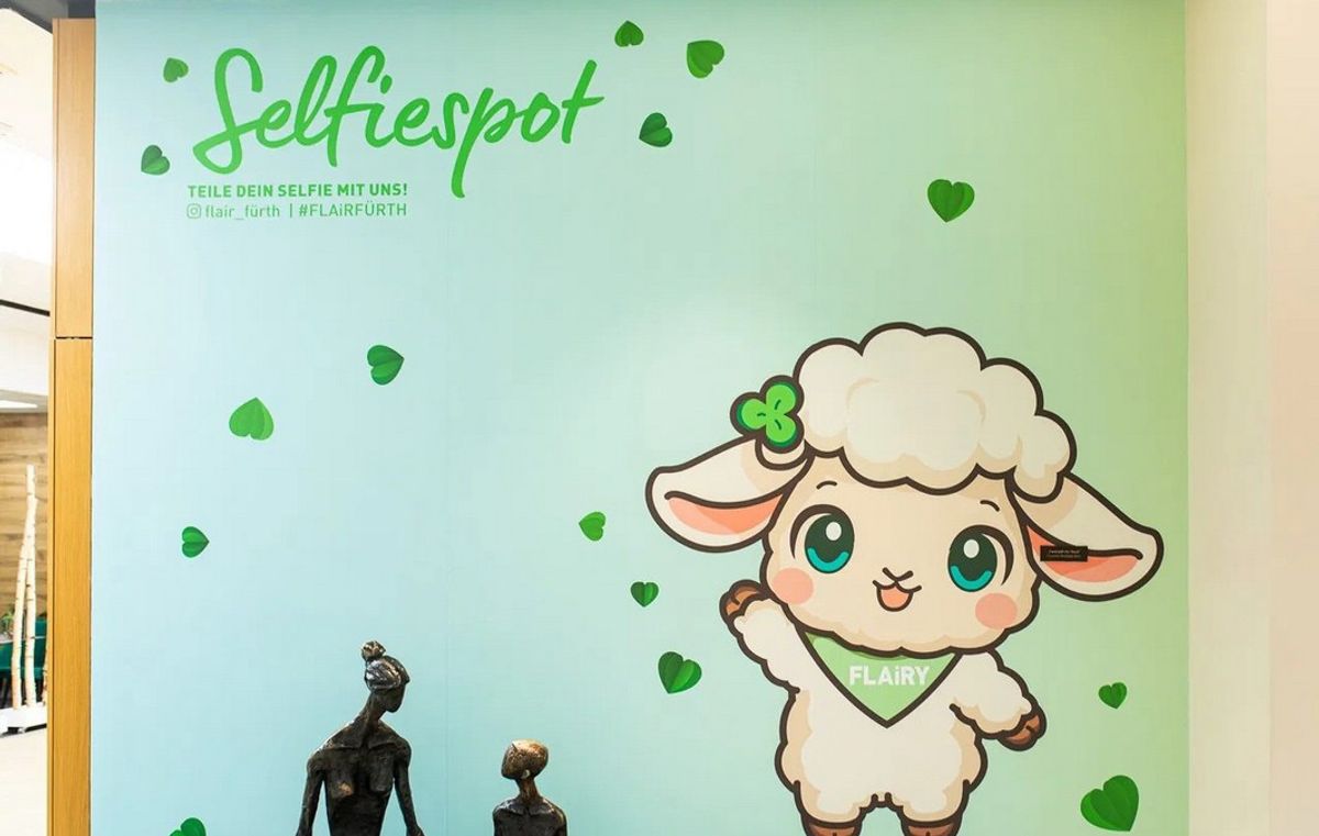 Selfiespot im FLAiR Fürth: türkisfarbene Wand mit winkendem Maskottchen FLAiRY, grünen Herzen und dem Schriftzug „Selfiespot“