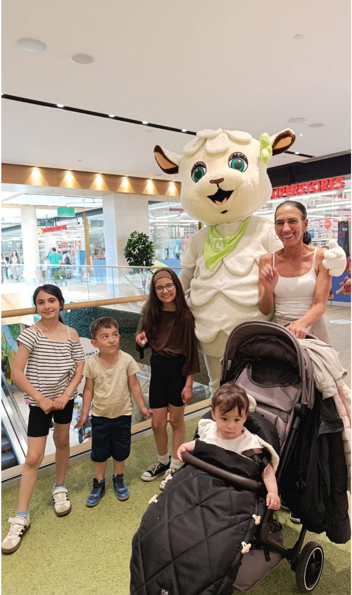 Maskottchen FLAiRY im Schafkostüm posiert mit einer Familie für ein Erinnerungsfoto im FLAiR Fürth