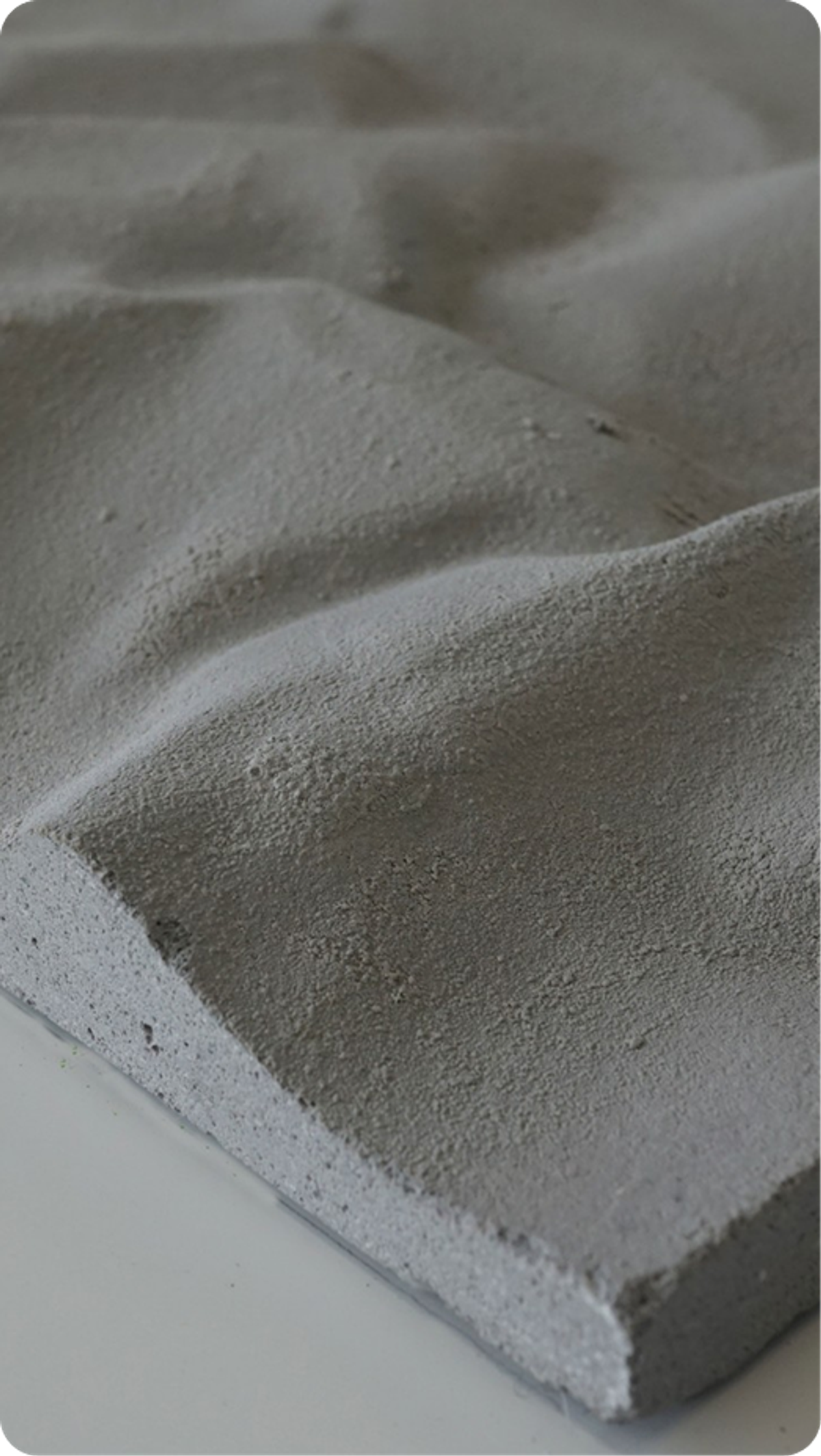 Nahaufnahme einer grauen Betonplatte mit wellenförmig strukturierter Oberfläche auf weißem Untergrund