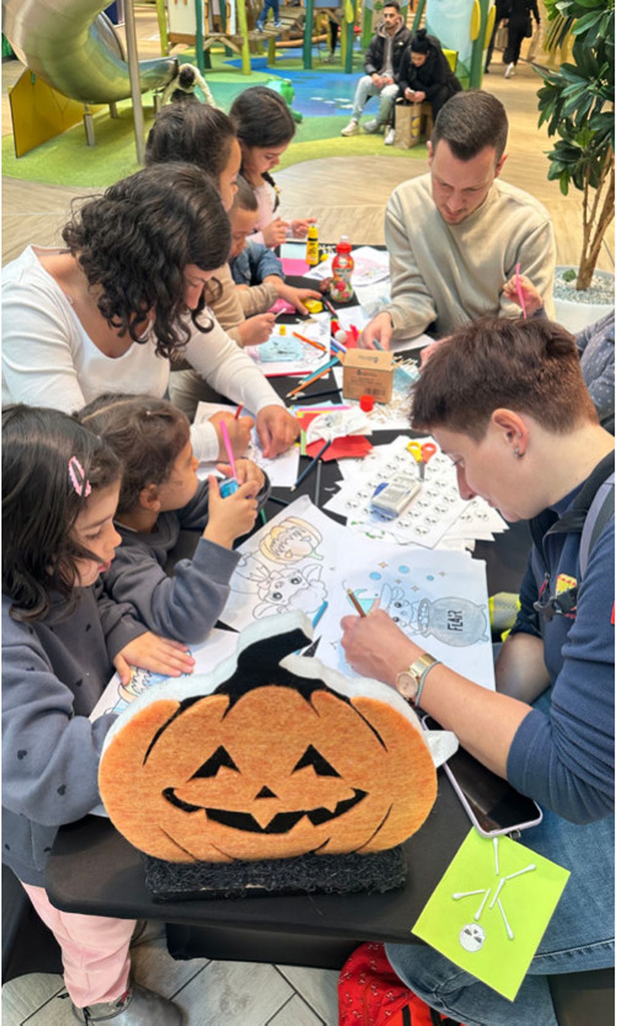Kinder und Eltern basteln an einem Tisch mit Kürbis-Deko Halloween-Motive im FLAiR Fürth