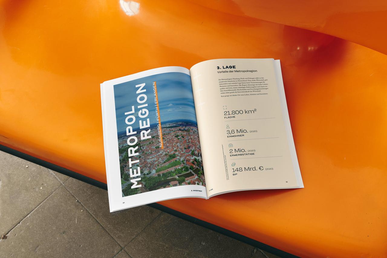 Aufgeschlagenes Central-Homes-Exposé auf orangefarbener Sitzbank, links Luftbild der Metropolregion Nürnberg, rechts Kennzahlen zur Lage