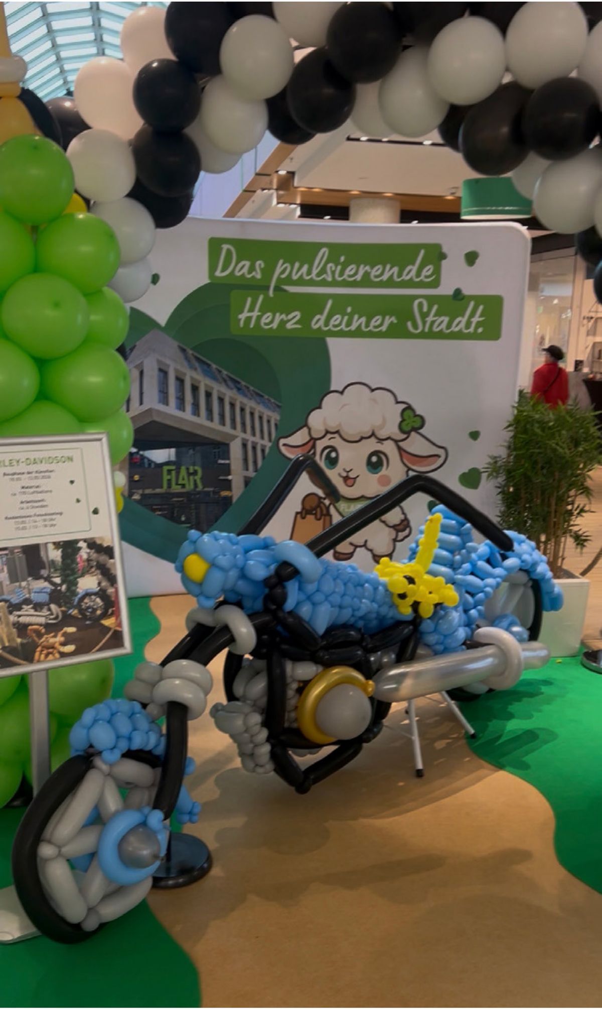 Aus Luftballons gebautes Motorrad mit FLAiRY-Figur vor einer grünen Rückwand im FLAiR Fürth