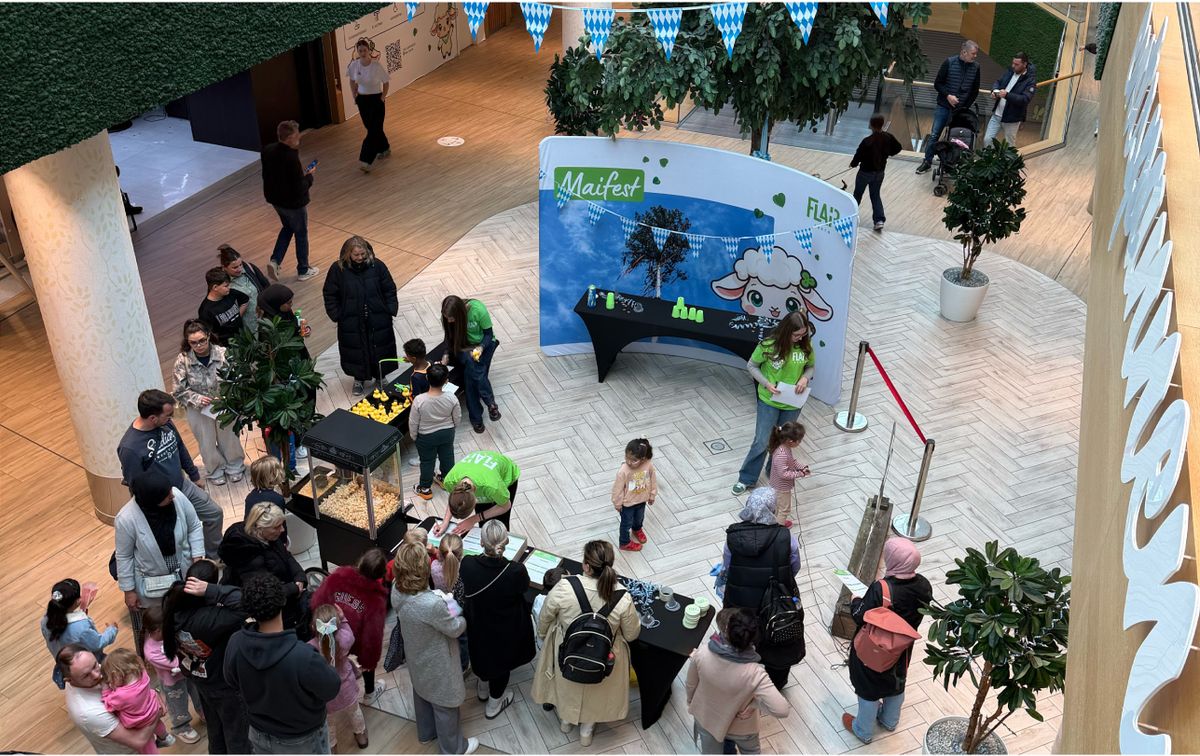 Blick von oben auf das Maifest im Atrium des FLAiR Fürth mit Spielstationen, Rückwand und vielen Familien