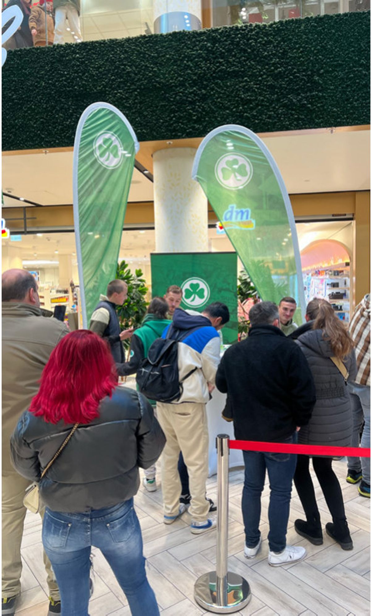 Besucher stehen im FLAiR Fürth Schlange für die Autogrammstunde der SpVgg Greuther Fürth, im Hintergrund grüne Kleeblatt-Beachflags