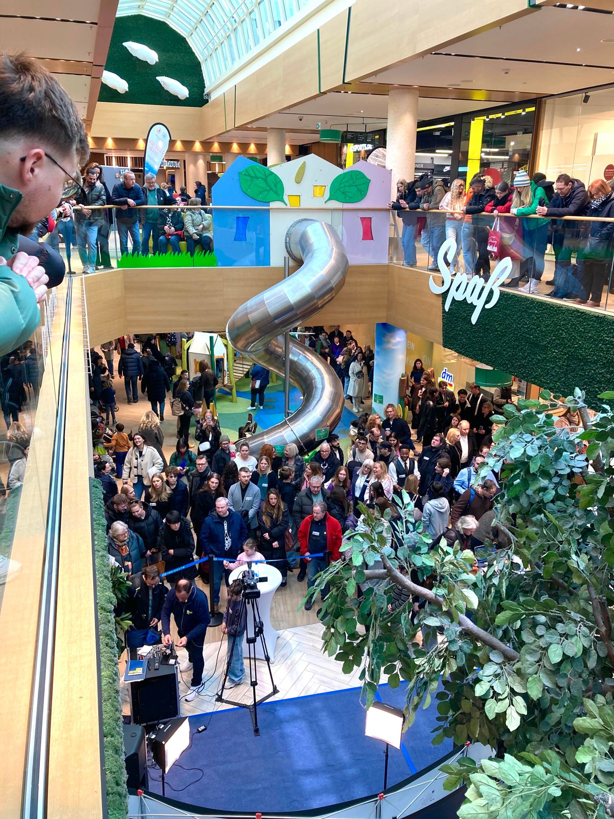 Eröffnung im FLAiR Fürth: dicht gedrängtes Publikum im Atrium vor der Edelstahlrutsche, Zuschauer an den Galerien, vorne eine Bühne mit Kamera und Scheinwerfern