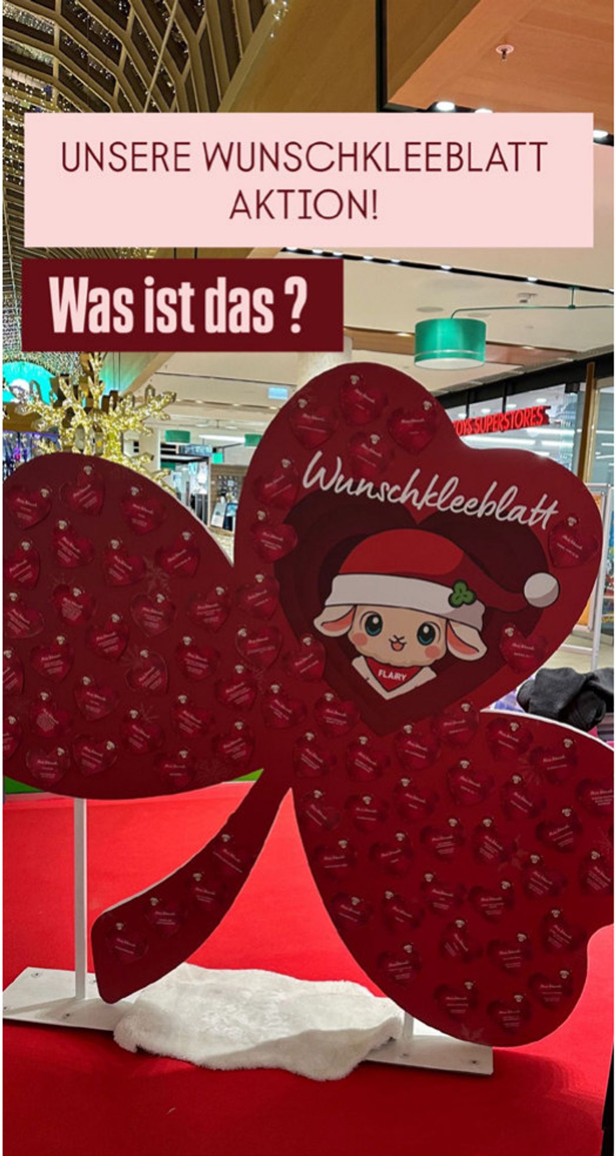 Großes rotes Wunschkleeblatt mit weihnachtlichem FLAiRY und Schild „Unsere Wunschkleeblatt-Aktion“
