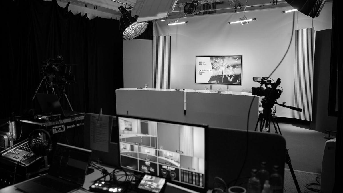 Regieplatz mit Multiview-Monitor vor einem Studioset mit Moderationstisch und Bildschirm