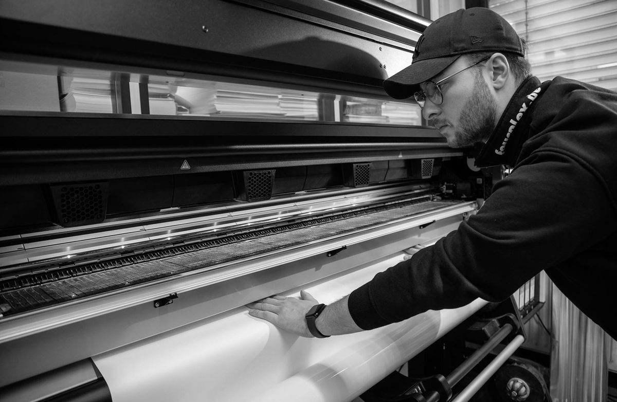Mitarbeiter von fourplex legt Material in den Großformatdrucker ein