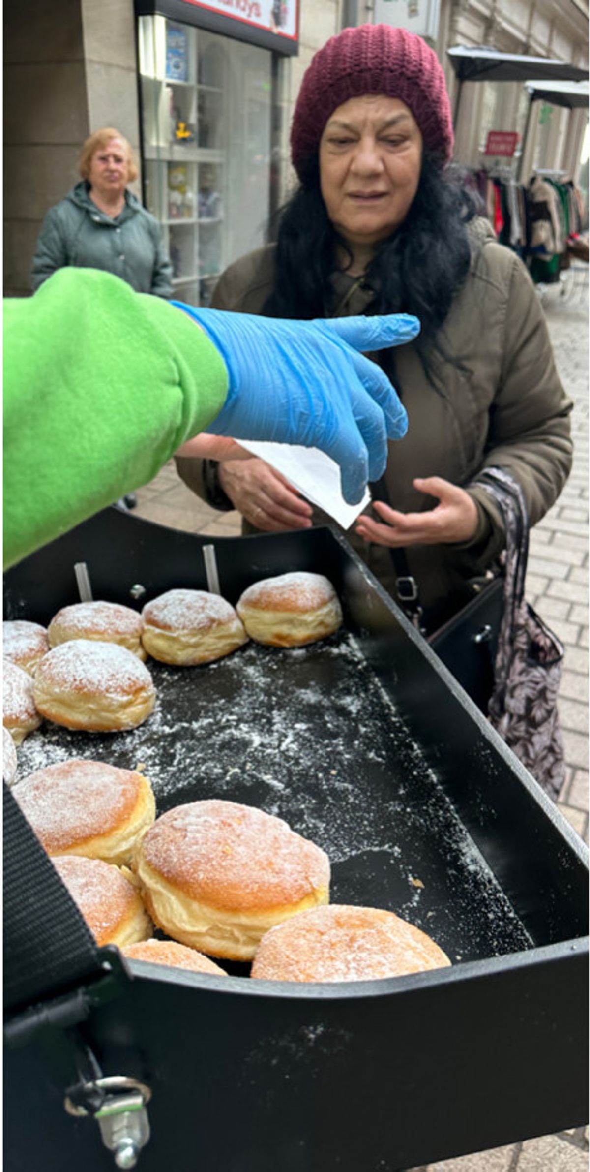 Promoterin im grünen Hoodie reicht einer Besucherin einen Krapfen aus dem Bauchladen