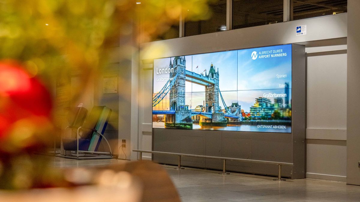 Videowand im Flughafenterminal mit London-Motiv und Tower Bridge, abendliche Aufnahme mit unscharfem Vordergrund