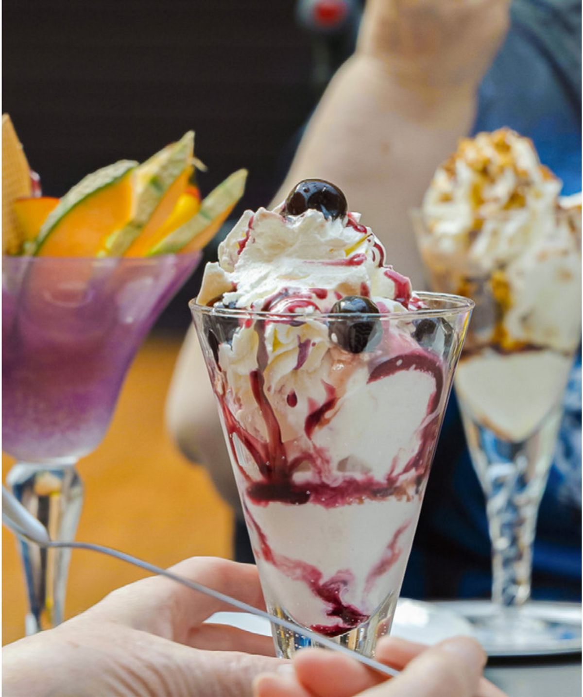 Hand hält einen Eisbecher mit Sahne und Früchten, daneben weitere Eisbecher, bei der Eisaktion für Seniorenheime im FLAiR Fürth
