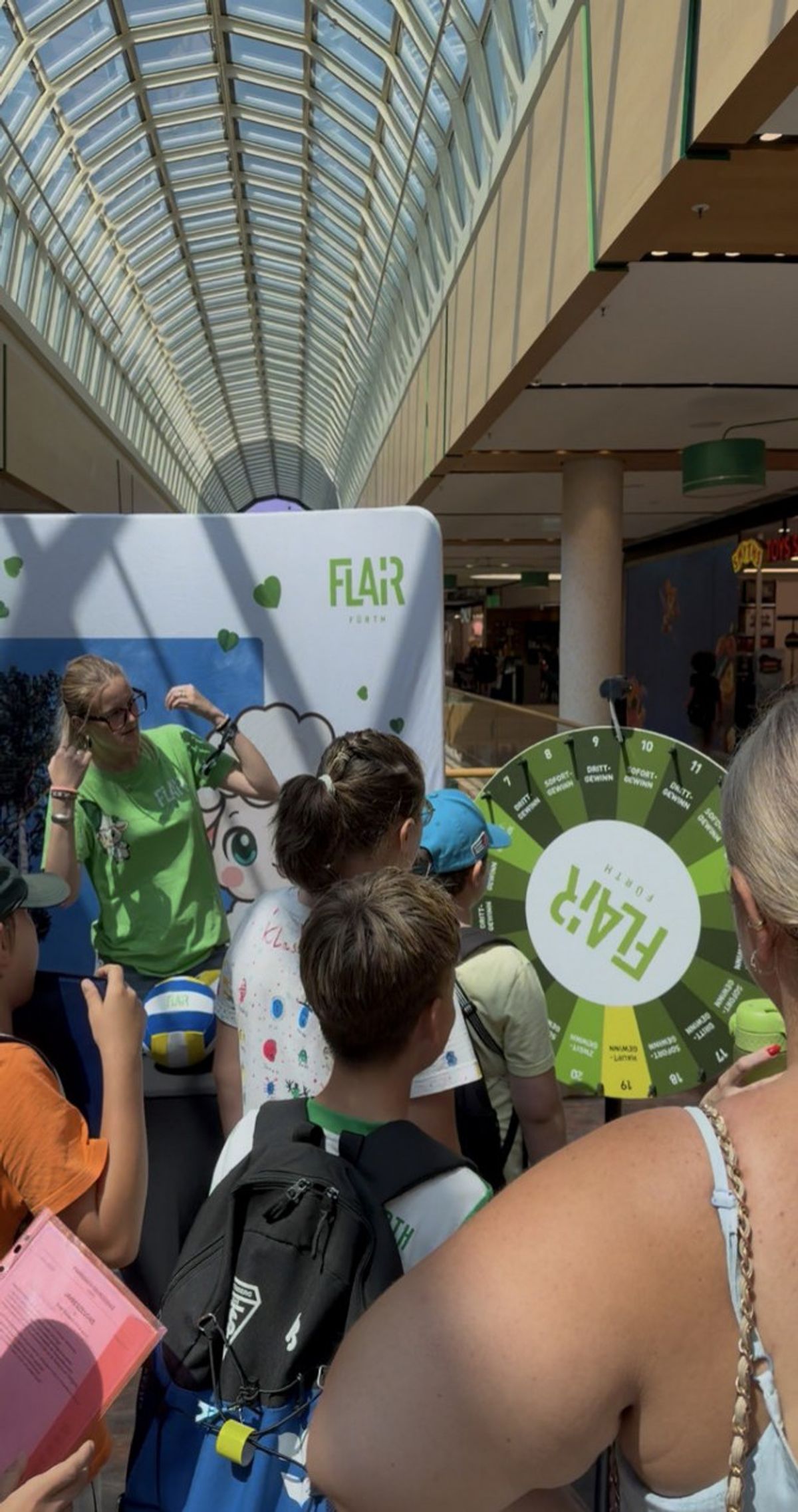 Schulkinder drehen am FLAiR-Glücksrad bei der Zeugnisaktion unter dem Glasdach